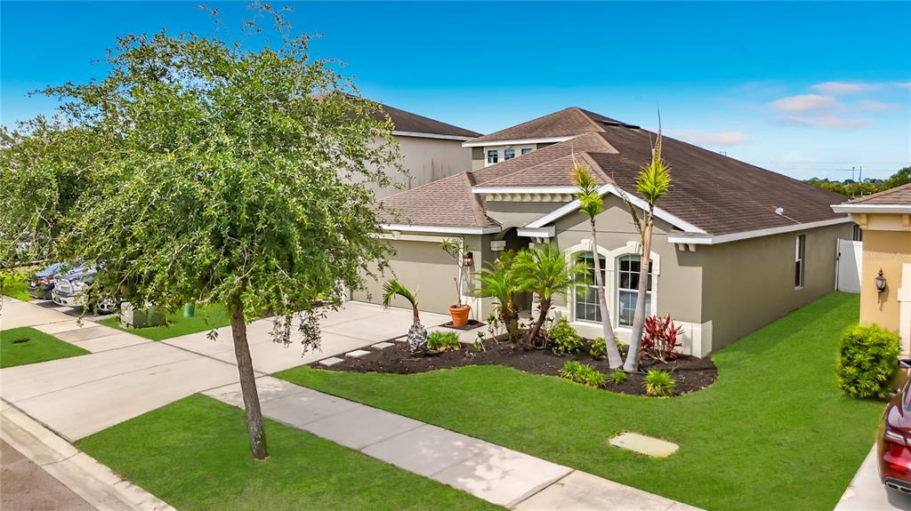 A single-story house with a tan exterior, a brown roof, and a landscaped front yard — 12033 GRAND KEMPSTON DRIVE, GIBSONTON, FL
