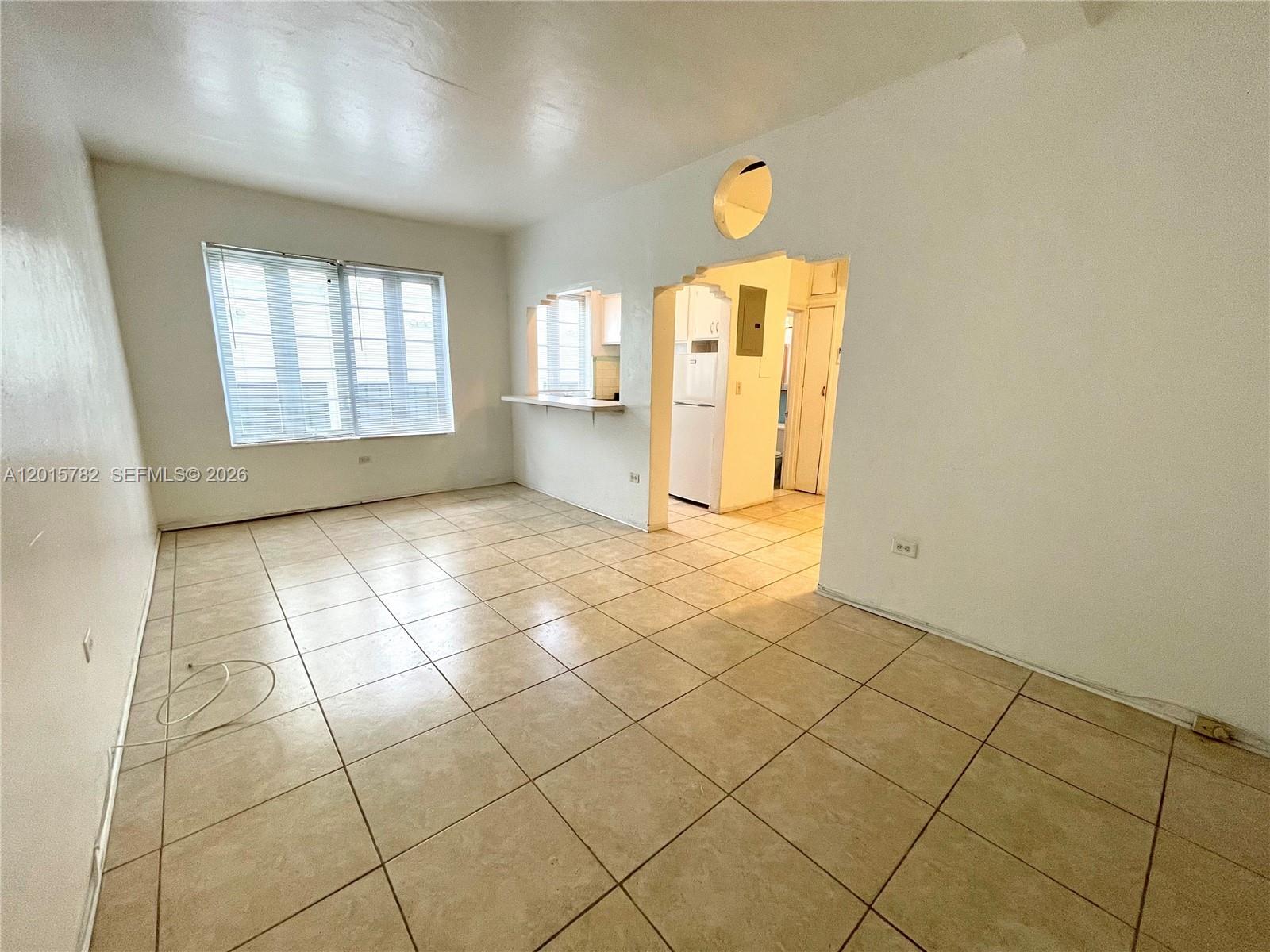 An empty room with beige tile flooring, white walls, and a pass-through to the kitchen — 901 Collins Ave # 103, Miami Beach FL 33139, MIAMI BEACH, FL