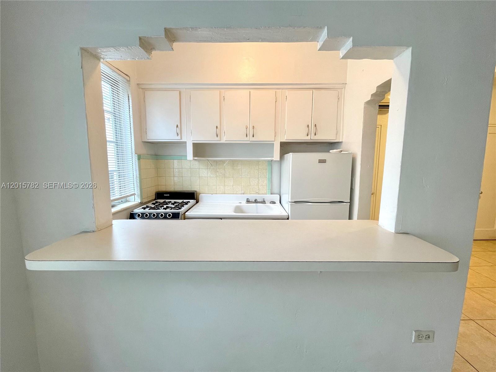 A kitchen with white cabinets and appliances is viewed through a cutout in the wall — 901 Collins Ave # 103, Miami Beach FL 33139, MIAMI BEACH, FL