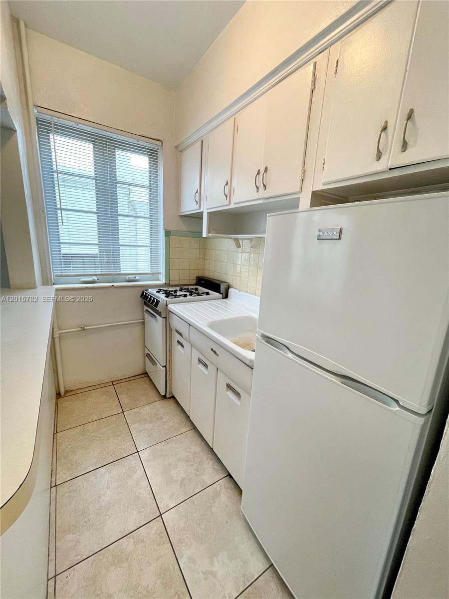A narrow kitchen features white cabinets, a white refrigerator, a gas stove, and tiled flooring — 901 Collins Ave # 103, Miami Beach FL 33139, MIAMI BEACH, FL