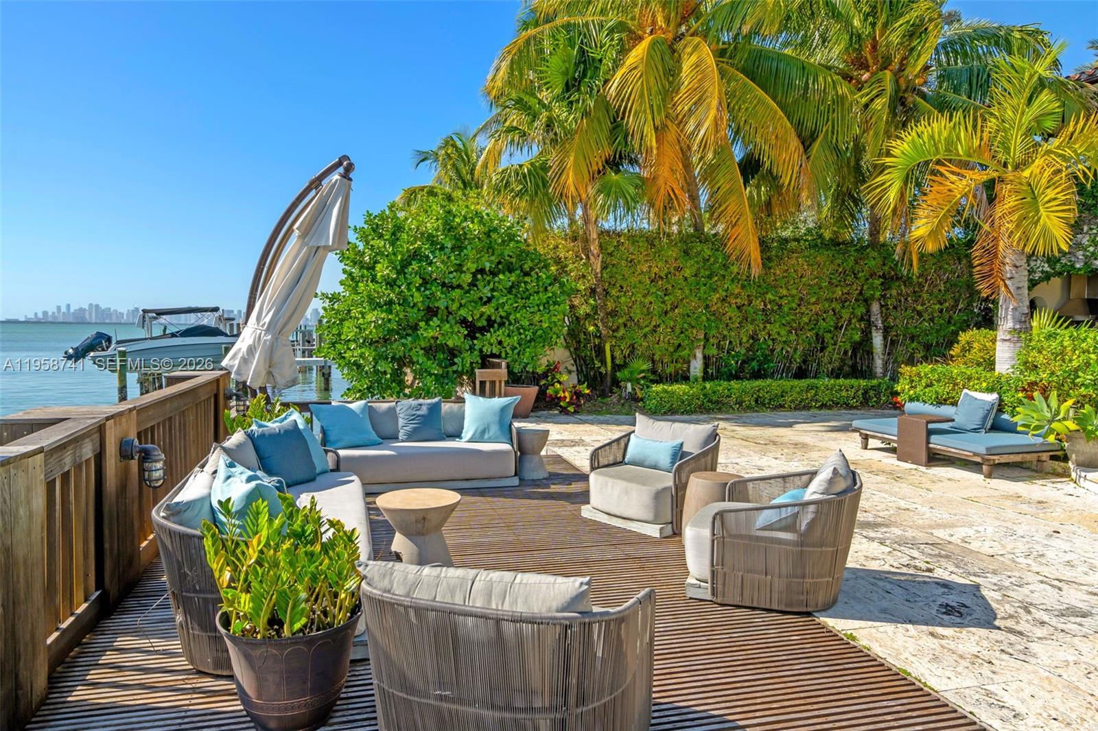 An outdoor patio features modern seating, a wooden deck, and a view of the water — 1398 Bay Dr, Miami Beach FL 33141, MIAMI BEACH, FL