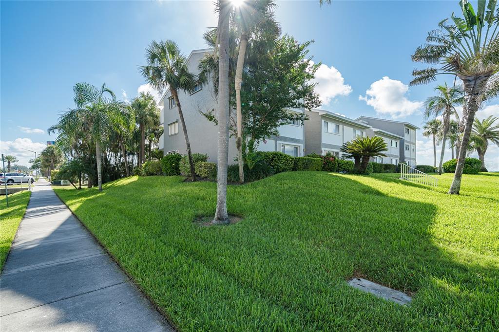 A sidewalk runs alongside a grassy lawn in front of a multi-story apartment building — 1301 GULF BOULEVARD UNIT 201, CLEARWATER BEACH, FL