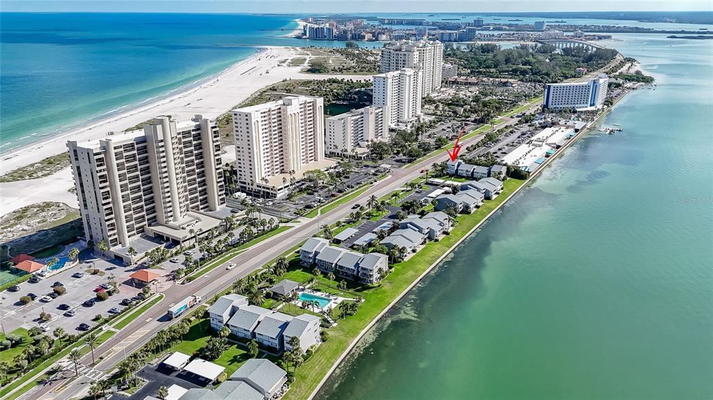 An aerial view shows a coastal resort area with multi-story buildings, parking lots, and beaches — 1301 GULF BOULEVARD UNIT 201, CLEARWATER BEACH, FL