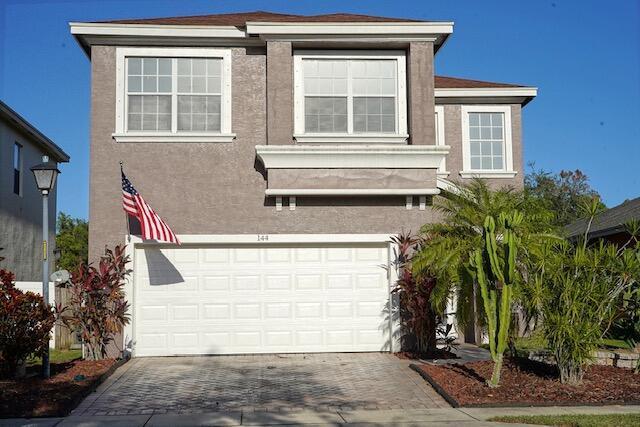A two-story house with a beige stucco exterior, a white garage door, and an American flag — 144 Blue Grotto Drive, Fort Pierce FL 34945, FORT PIERCE, FL