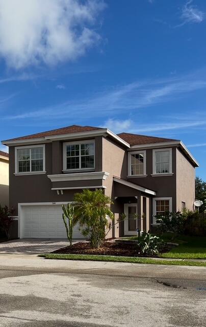 A two-story suburban house with a brown stucco exterior, a two-car garage, and landscaping — 144 Blue Grotto Drive, Fort Pierce FL 34945, FORT PIERCE, FL