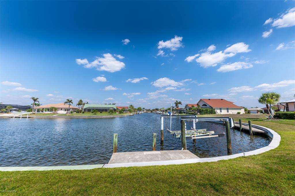 A concrete dock and boat lift extend into a canal surrounded by residential homes — 2572 BRAZILIA COURT, PUNTA GORDA, FL