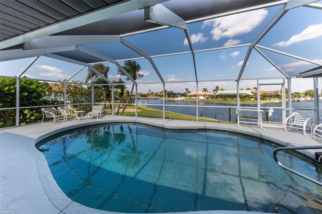 A screened-in swimming pool overlooks a canal with houses in the background — 2572 BRAZILIA COURT, PUNTA GORDA, FL