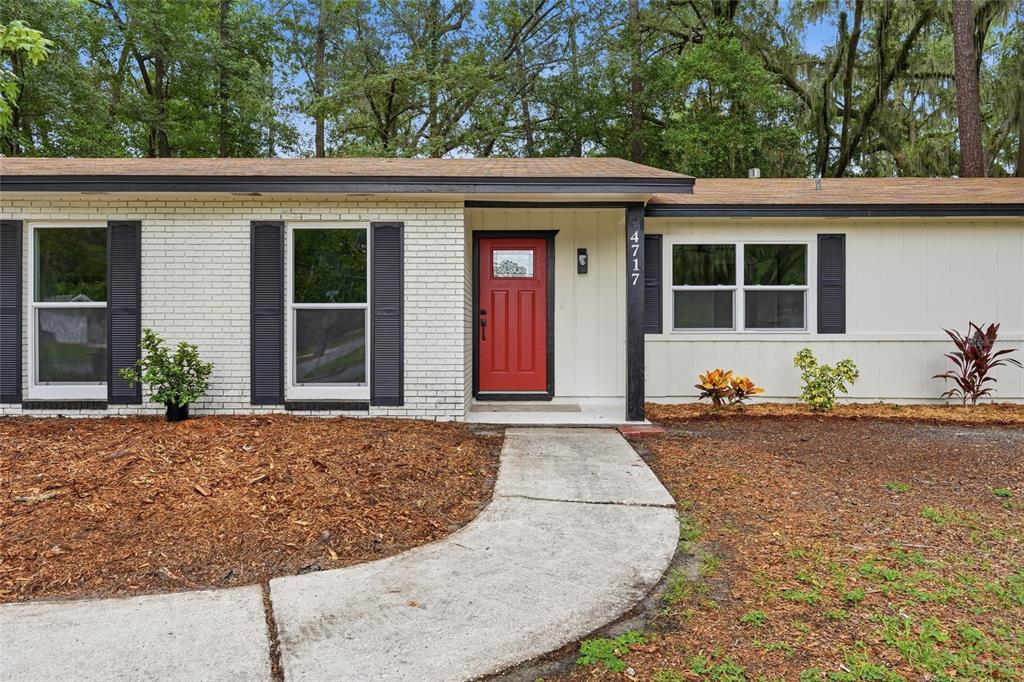 A single-story house features a white brick and siding exterior with a red front door — 4717 NW 31ST TERRACE, GAINESVILLE, FL