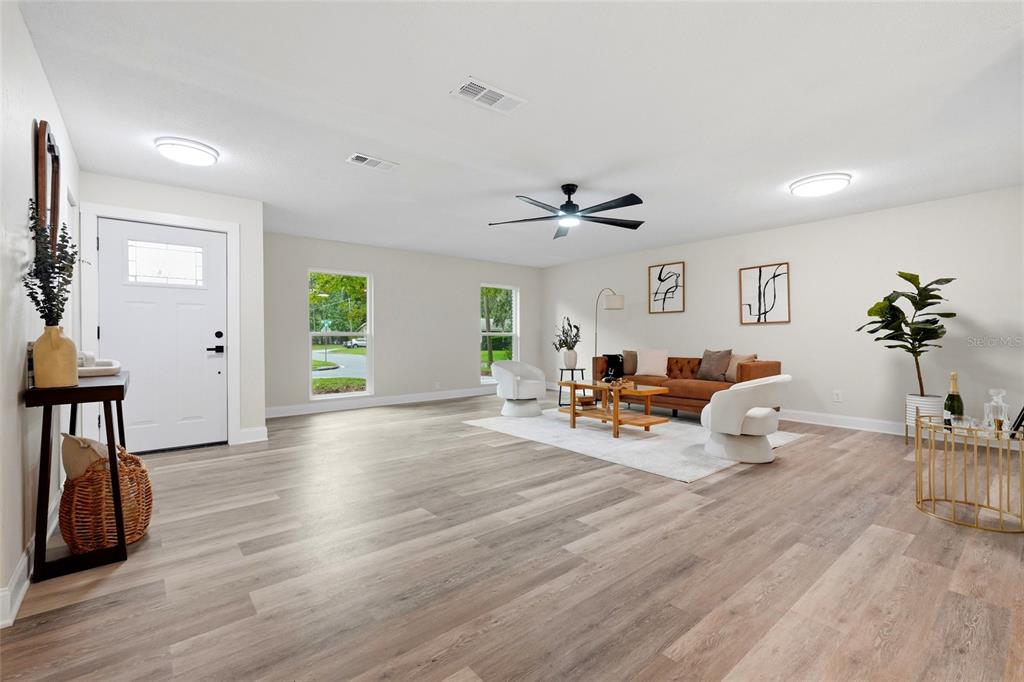 A bright living room features light wood-look flooring, a brown sofa, and two white chairs — 4717 NW 31ST TERRACE, GAINESVILLE, FL
