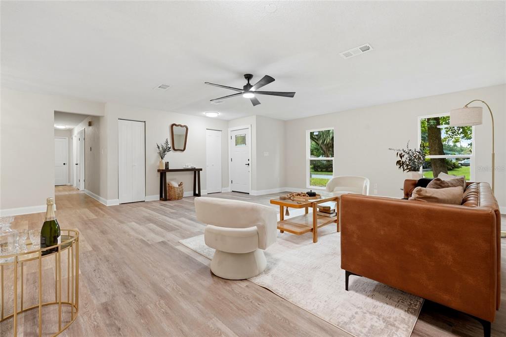 A living room features light wood-look flooring, a leather sofa, two cream chairs, and a ceiling fan — 4717 NW 31ST TERRACE, GAINESVILLE, FL