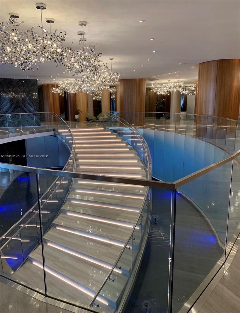 A grand curved staircase with illuminated steps sits in a lobby featuring modern light fixtures — 488 NE 18TH # 2703, Miami FL 33132, MIAMI, FL