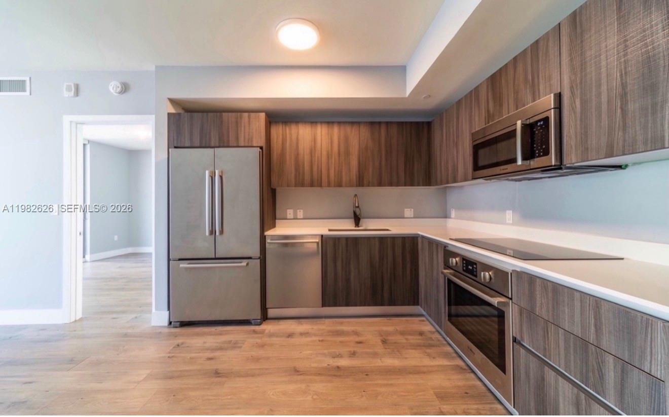A modern kitchen features wood-grain cabinets, stainless steel appliances, and light-colored countertops — 488 NE 18TH # 2703, Miami FL 33132, MIAMI, FL