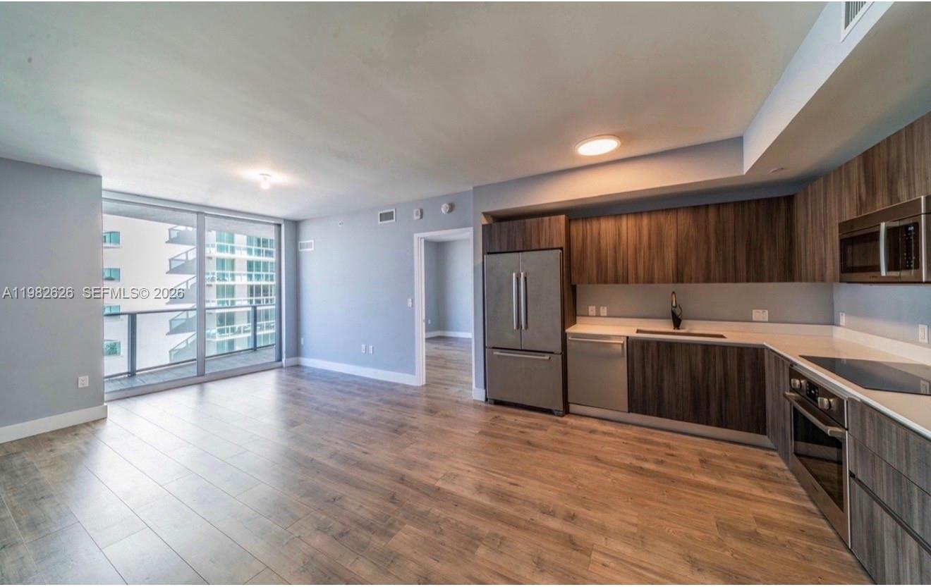 An open-concept kitchen and living area featuring wood-look flooring, stainless steel appliances, and balcony access — 488 NE 18TH # 2703, Miami FL 33132, MIAMI, FL