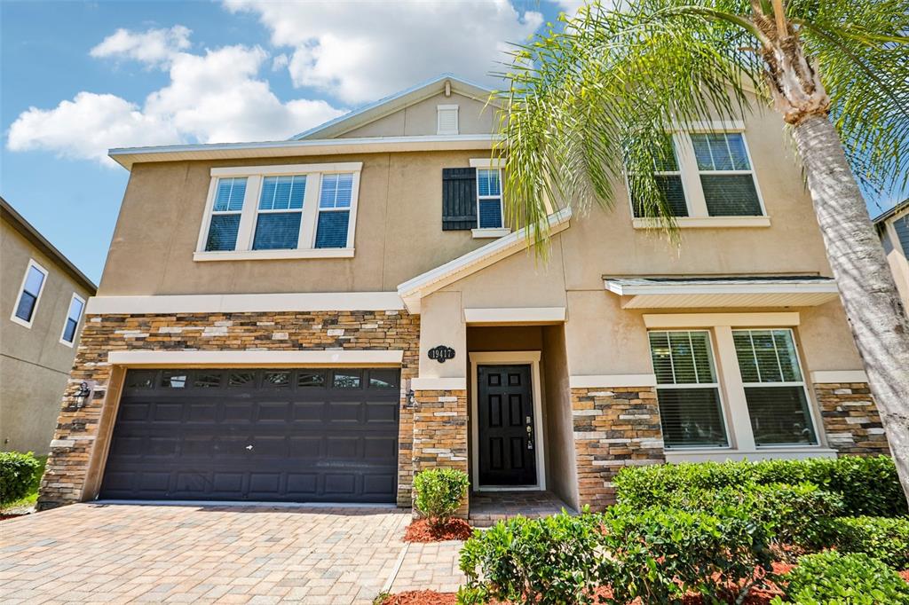 A two-story house with a stone facade, a dark garage door, and a palm tree — 19417 PADDOCK VIEW DRIVE, TAMPA, FL