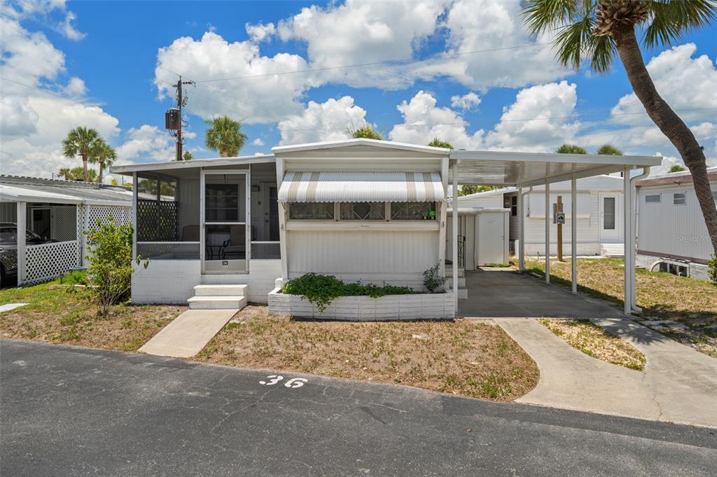 A single-story mobile home with a screened porch, carport, and white siding under a blue sky — 4851 W GANDY BOULEVARD UNIT B9L36, TAMPA, FL