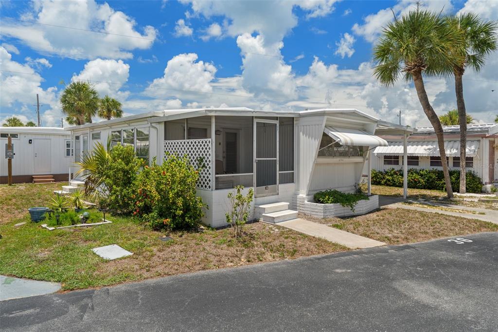 A white mobile home with a screened-in porch and palm trees under a cloudy sky — 4851 W GANDY BOULEVARD UNIT B9L36, TAMPA, FL