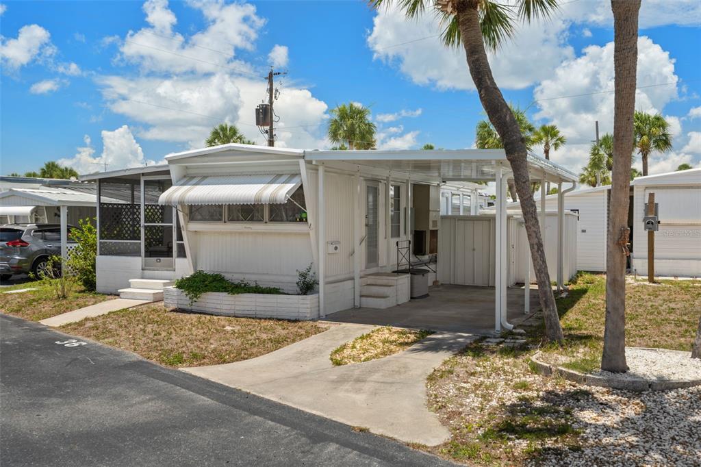 A single-story mobile home with a carport, screened porch, and white siding under a blue sky — 4851 W GANDY BOULEVARD UNIT B9L36, TAMPA, FL