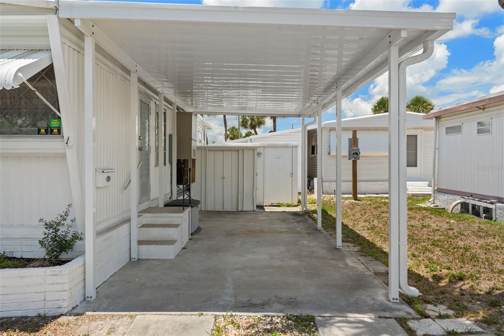 A concrete carport with a white metal roof is attached to a mobile home exterior — 4851 W GANDY BOULEVARD UNIT B9L36, TAMPA, FL
