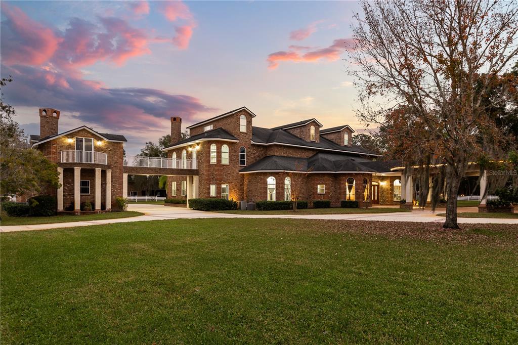 A large brick house with a bridge connecting two sections under a sunset sky — 1501 LAKE MARKHAM ROAD, SANFORD, FL