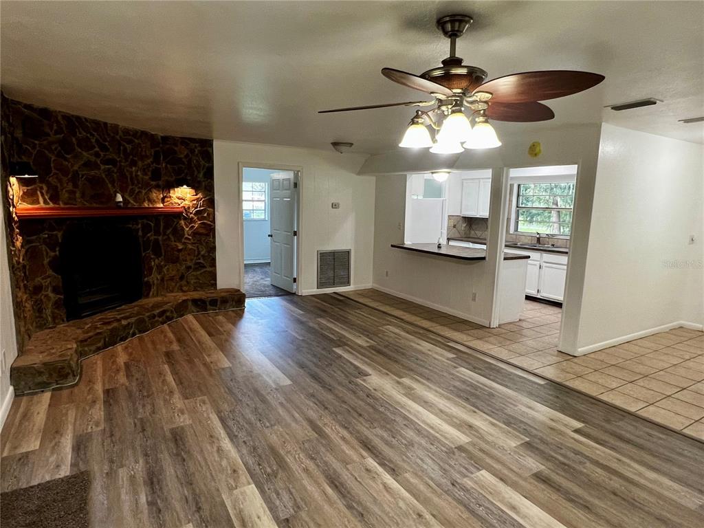 A living room with wood-look flooring, a stone fireplace, and an open kitchen with tile — 2948 NE 14TH AVENUE, OCALA, FL
