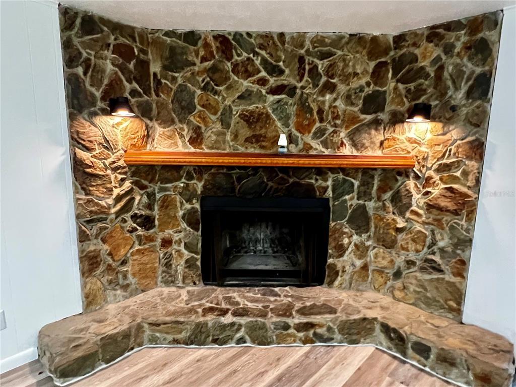 A stone fireplace with a wooden mantel sits in a room with wood-look flooring — 2948 NE 14TH AVENUE, OCALA, FL