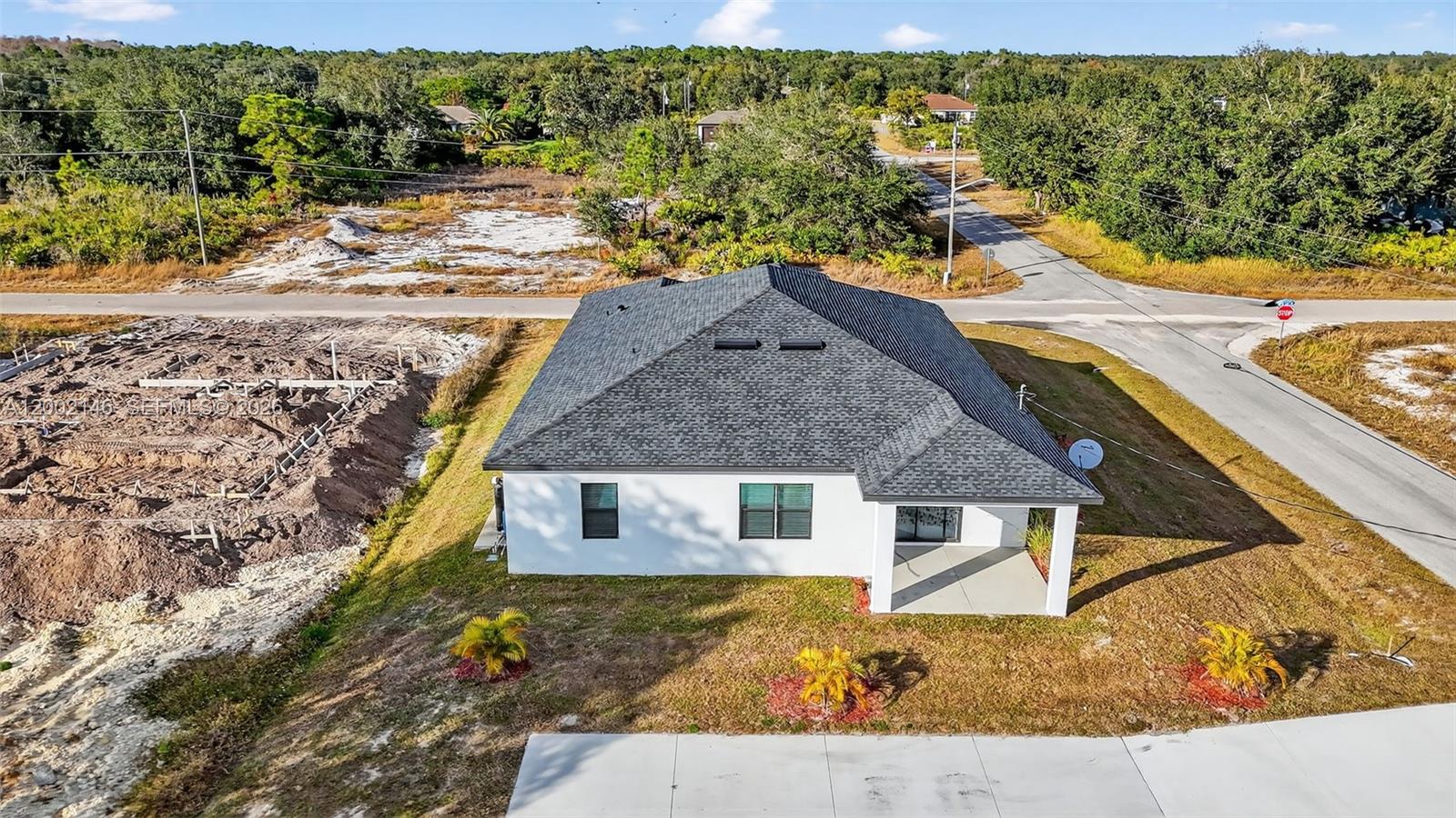 An aerial view shows a white house with a dark roof next to a construction site — 2513 69TH ST W, Lehigh Acres FL 33971, LEHIGH ACRES, FL