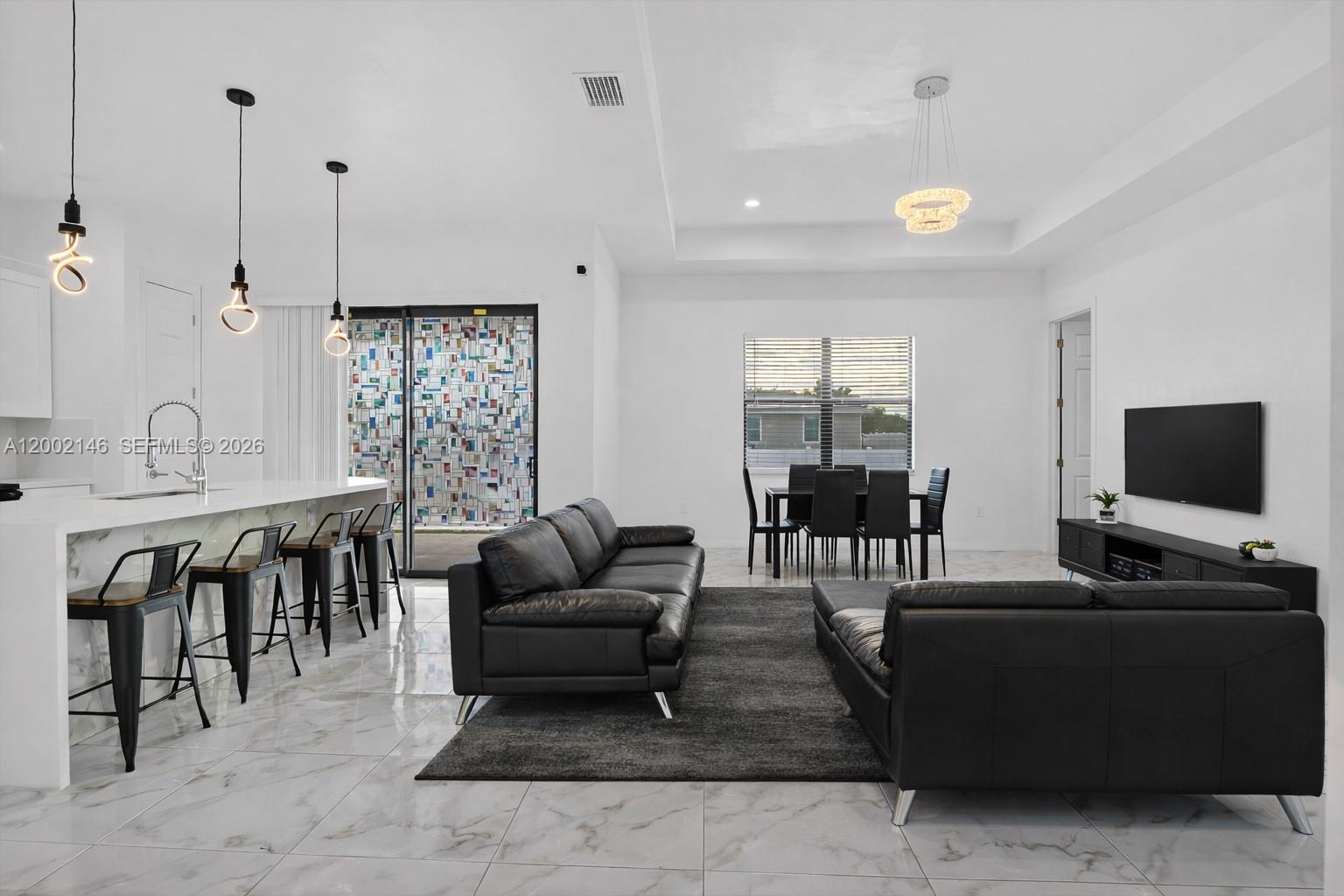 A modern open-concept living and dining area features white marble floors, black leather furniture, and pendant lighting — 2513 69TH ST W, Lehigh Acres FL 33971, LEHIGH ACRES, FL
