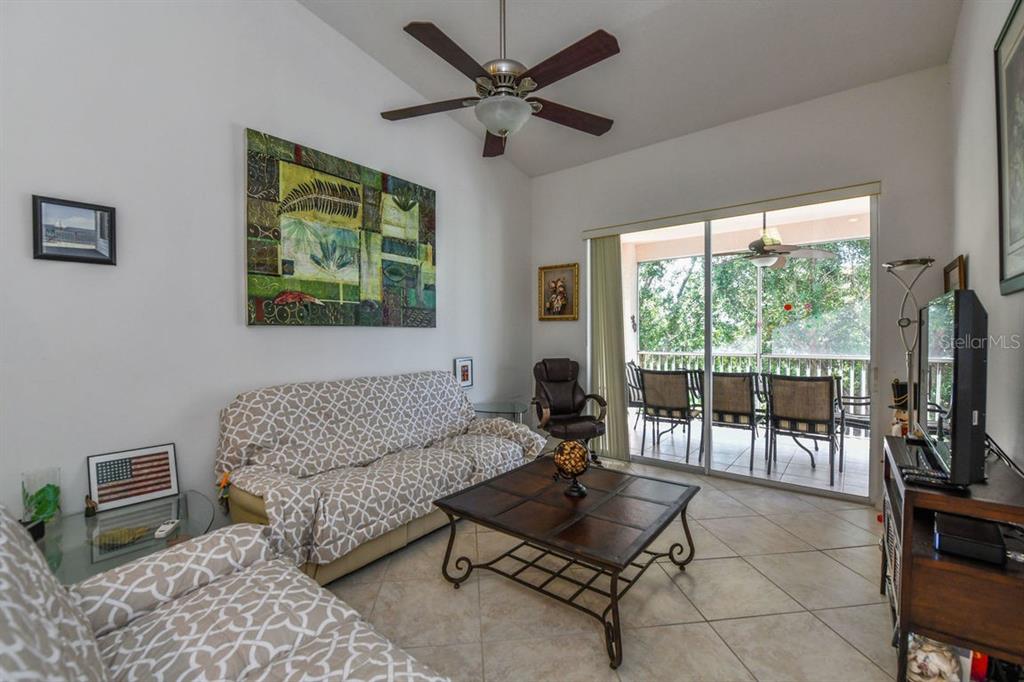 A living room with tile floors, a ceiling fan, patterned sofa covers, and a sliding door — 4228 CENTRAL SARASOTA PARKWAY UNIT 1024, SARASOTA, FL