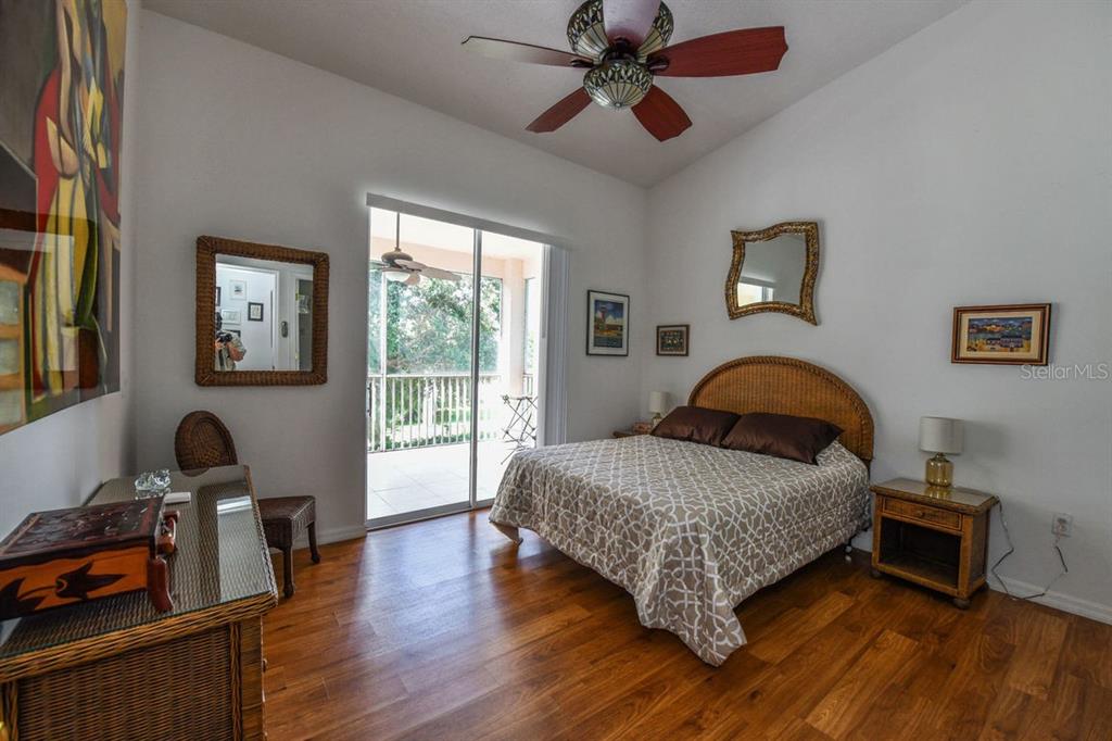 A bedroom features a wicker headboard, wood flooring, a ceiling fan, and a sliding glass door — 4228 CENTRAL SARASOTA PARKWAY UNIT 1024, SARASOTA, FL