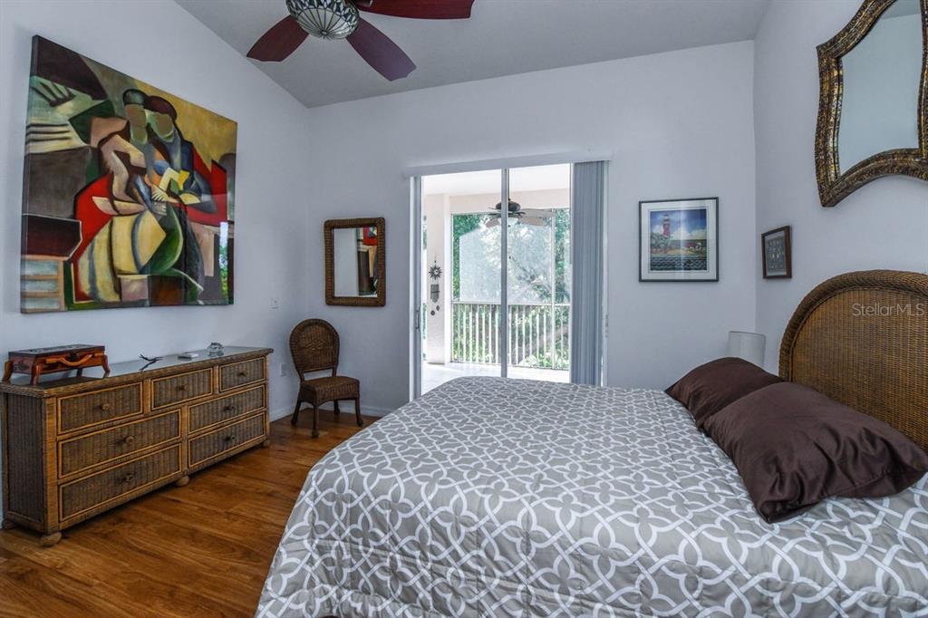 A bedroom features a patterned bedspread, a wicker dresser, a large abstract painting, and a balcony — 4228 CENTRAL SARASOTA PARKWAY UNIT 1024, SARASOTA, FL