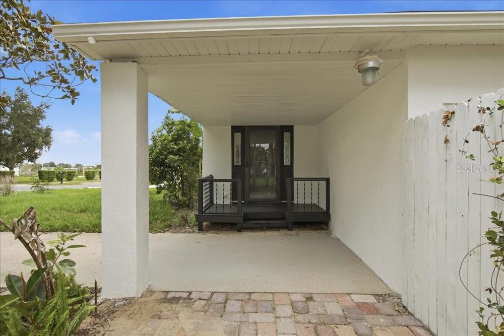 A covered entryway features a concrete floor, a small dark wooden deck, and a screen door — 171 STANLEY BELL DRIVE, MOUNT DORA, FL