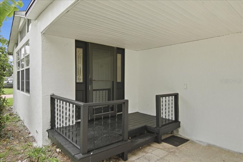 A covered entryway features a dark wooden deck with railings leading to a front door — 171 STANLEY BELL DRIVE, MOUNT DORA, FL