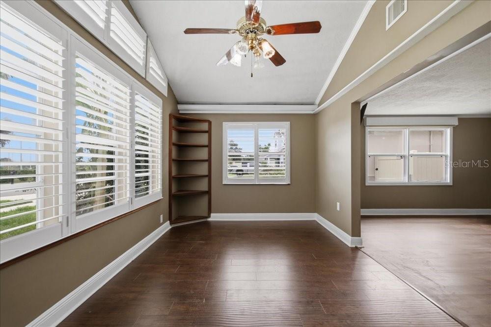 A room with dark wood floors, a ceiling fan, plantation shutters, and a corner bookshelf — 171 STANLEY BELL DRIVE, MOUNT DORA, FL