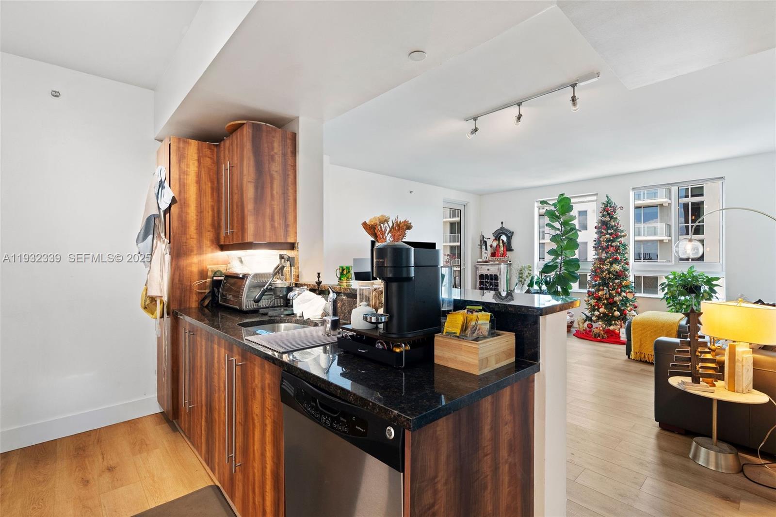 A kitchen with wood cabinets and black countertops opens into a living area with a tree — 7350 SW 89th St # 1110S, Miami FL 33156, MIAMI, FL