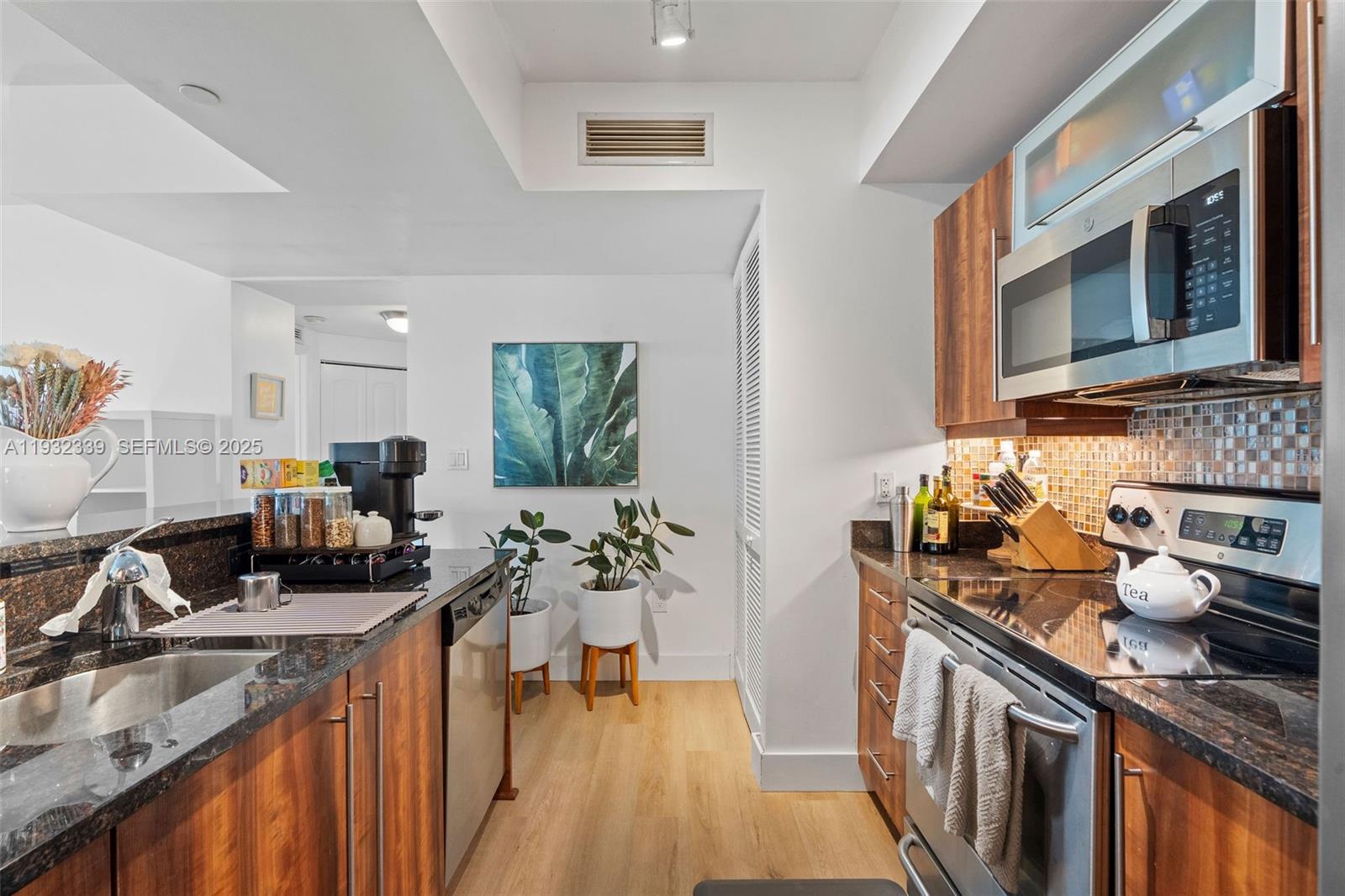 A galley kitchen features wood-toned cabinetry, dark granite countertops, stainless steel appliances, and light flooring — 7350 SW 89th St # 1110S, Miami FL 33156, MIAMI, FL