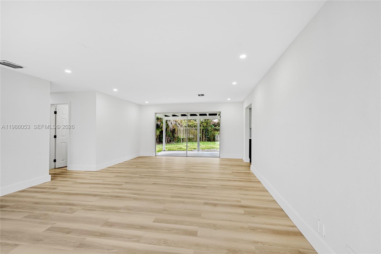 A bright, empty living room features white walls, light wood-look flooring, and sliding glass doors — 1353 NW 62nd Way, Margate FL 33063, MARGATE, FL