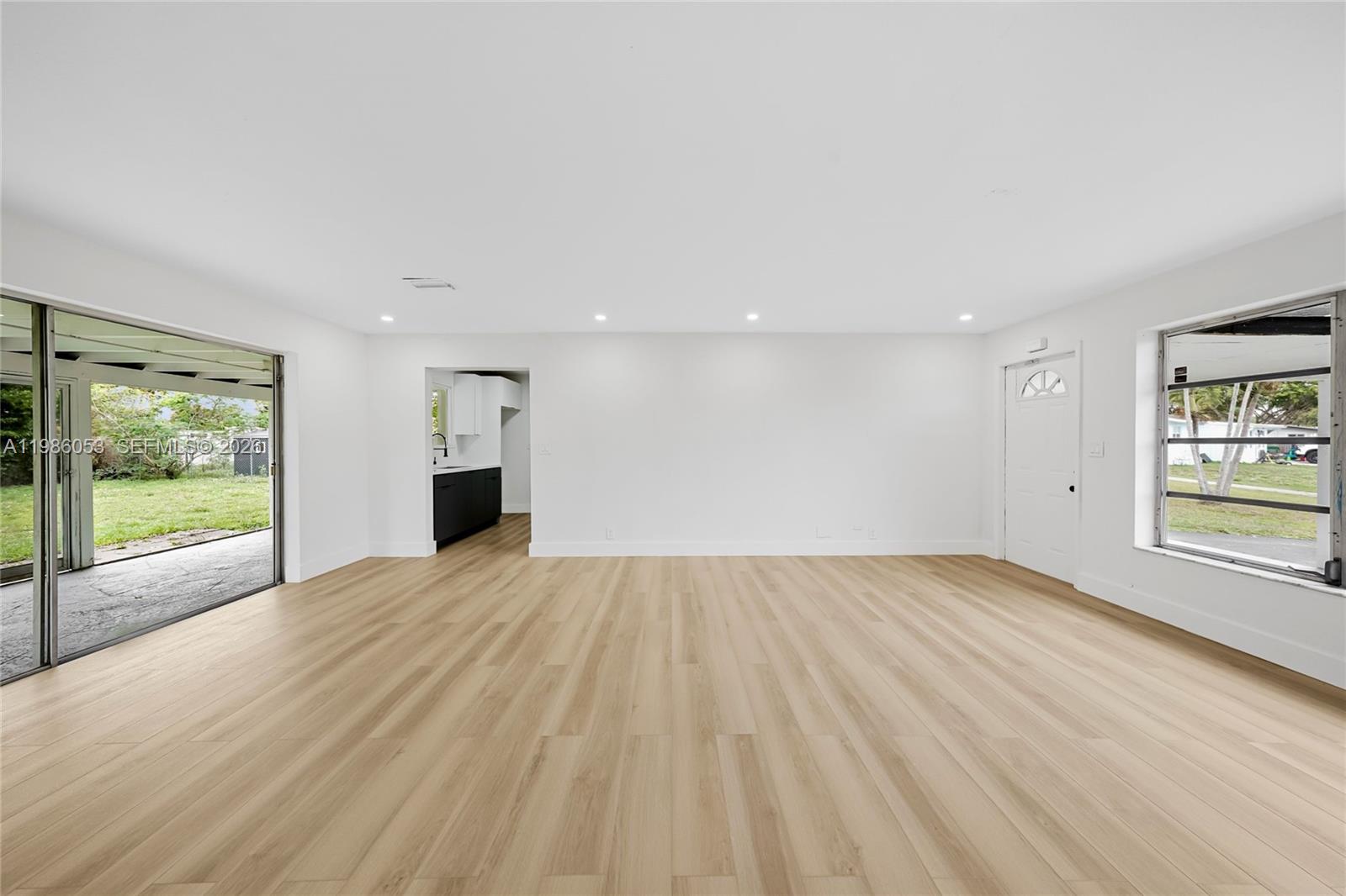 An empty living room features light wood-look flooring, white walls, and a sliding glass door — 1353 NW 62nd Way, Margate FL 33063, MARGATE, FL