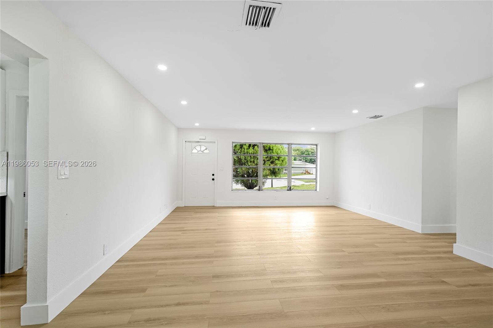 A bright, empty living room features white walls, recessed lighting, and light wood-look flooring — 1353 NW 62nd Way, Margate FL 33063, MARGATE, FL