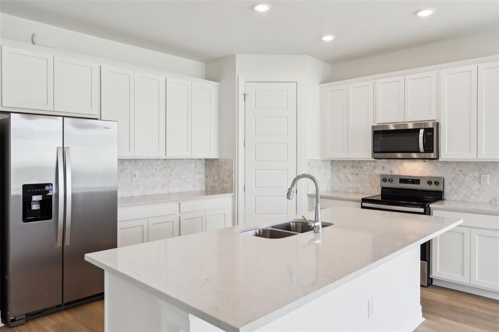 A modern kitchen features white cabinetry, stainless steel appliances, a center island, and light countertops — 16672 EXPEDITION COURT, PUNTA GORDA, FL
