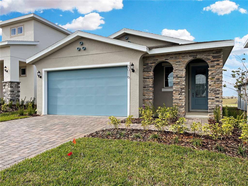A single-story house with a blue garage door, stone facade, and a paved driveway — 2016 SUNSHINE PEAK DRIVE, MINNEOLA, FL