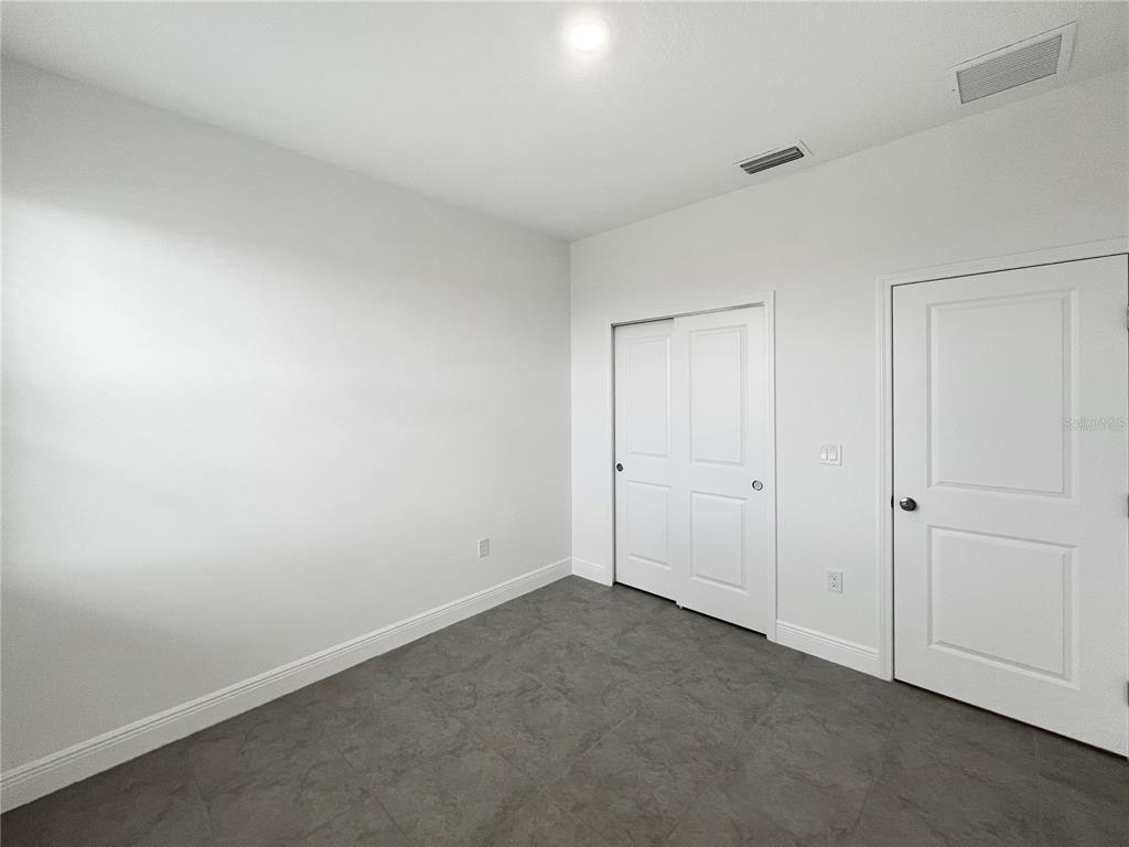 A bedroom with white walls, gray tile flooring, a sliding closet, and a door — 2016 SUNSHINE PEAK DRIVE, MINNEOLA, FL