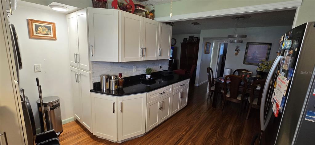 A kitchen features white cabinets, black countertops, and wood-look flooring, opening into a dining area — 3894 37TH STREET S UNIT 41, ST PETERSBURG, FL