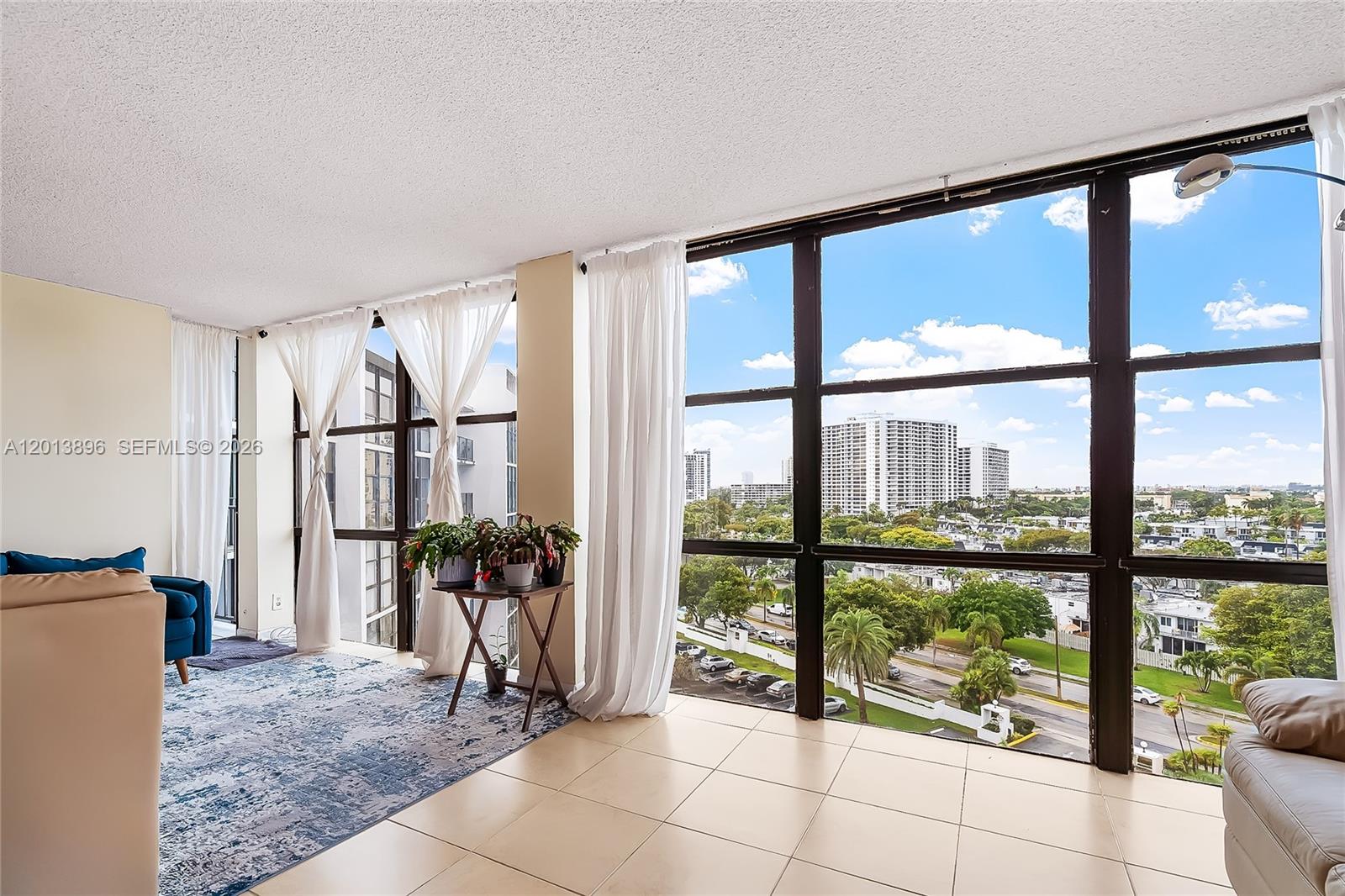 A living room with tile floors, a patterned rug, and floor-to-ceiling windows overlooking a city — 800 Parkview Dr # 901, Hallandale Beach FL 33009, HALLANDALE BEACH, FL