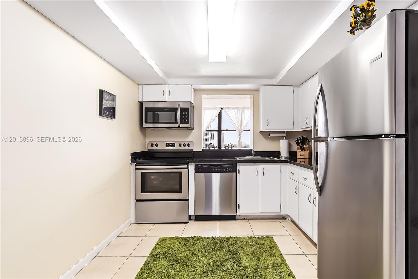 A kitchen features white cabinets, stainless steel appliances, black countertops, and a green area rug — 800 Parkview Dr # 901, Hallandale Beach FL 33009, HALLANDALE BEACH, FL