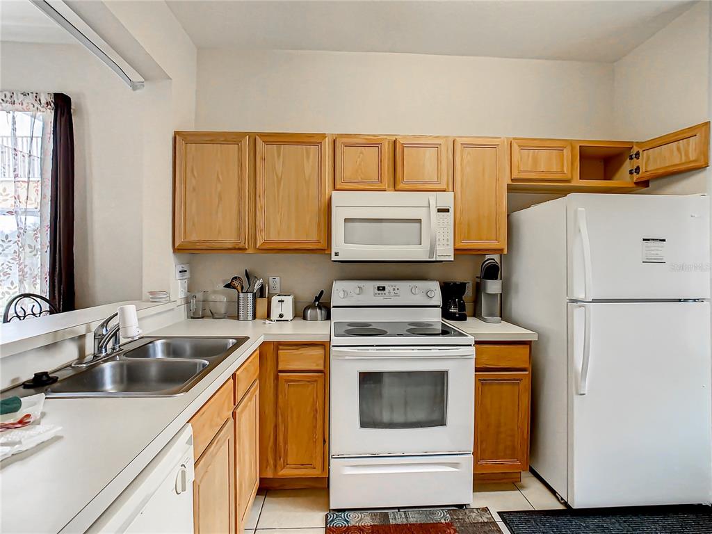 A kitchen features light wood cabinets, white appliances, a double sink, and tiled flooring — 702 CALABRIA AVE, DAVENPORT, FL