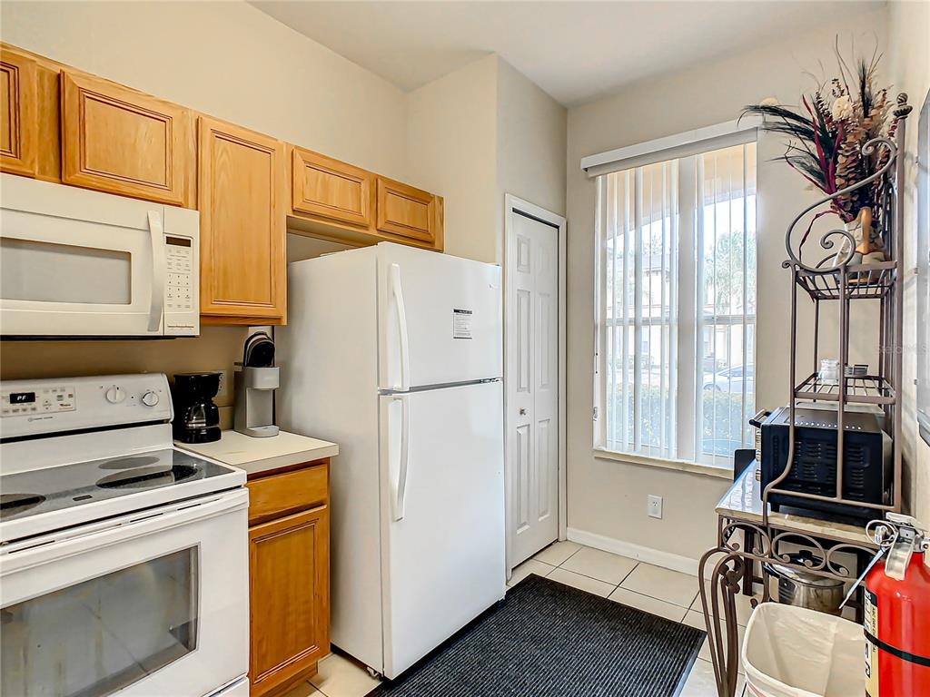 A kitchen features light wood cabinets, white appliances, a window with vertical blinds, and tile flooring — 702 CALABRIA AVE, DAVENPORT, FL