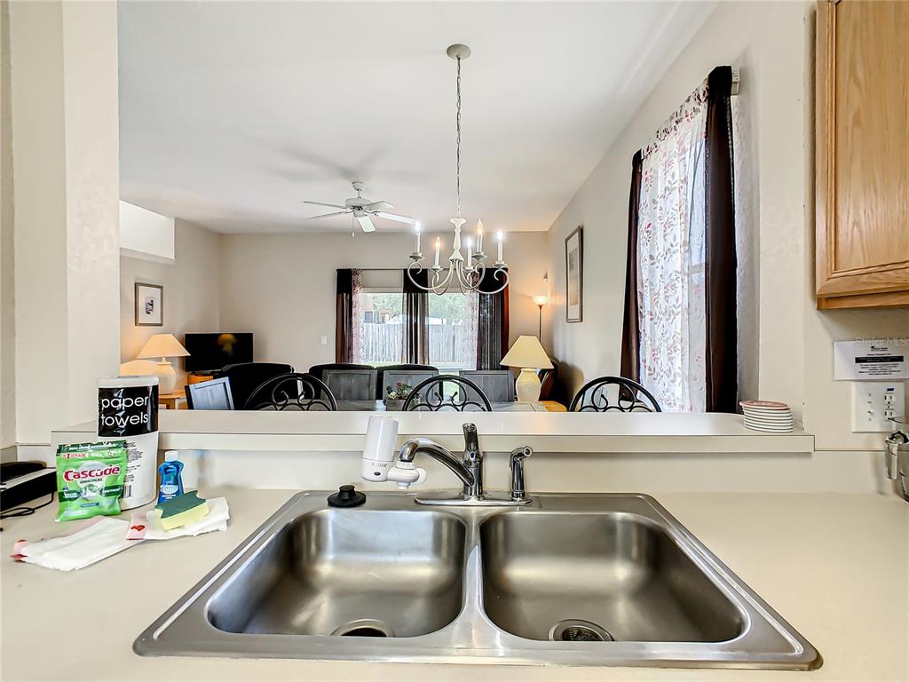 A kitchen sink overlooks a dining area with a chandelier and a ceiling fan — 702 CALABRIA AVE, DAVENPORT, FL