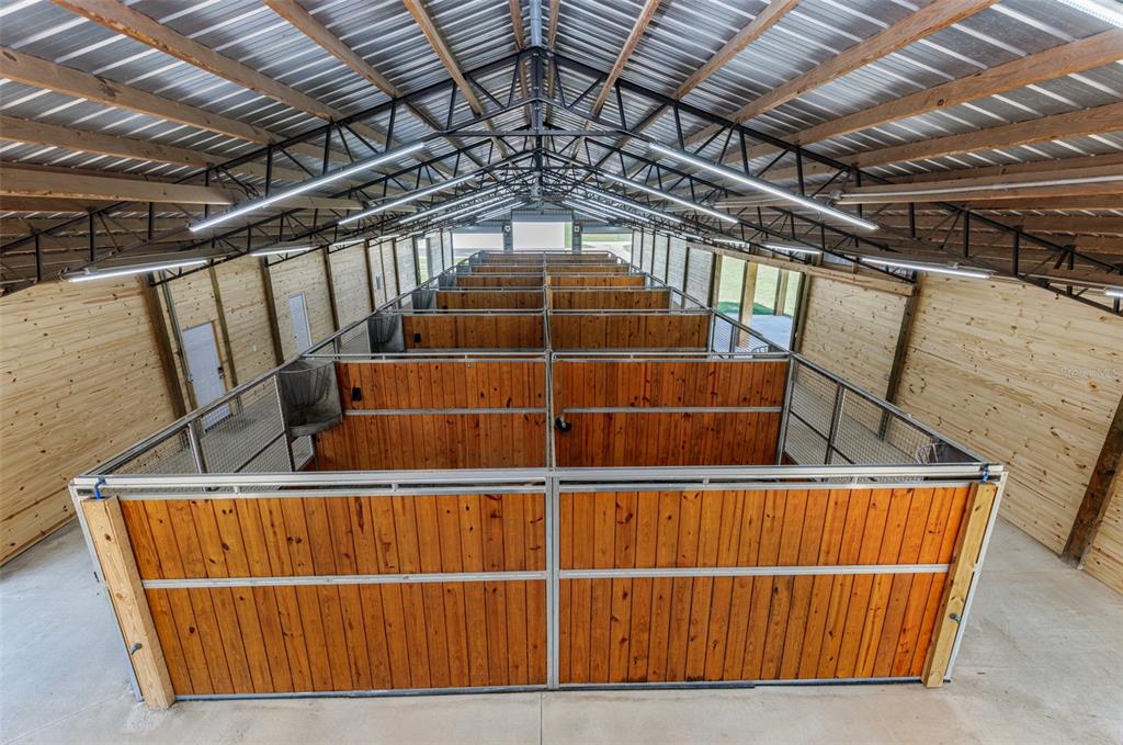 An elevated view of a horse barn interior featuring multiple wooden stalls and metal trusses — 1285 NW 102ND A BOULEVARD, WILDWOOD, FL