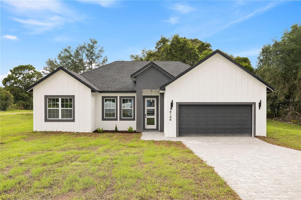 A single-story house with white board-and-batten siding, a dark gray garage, and a paved driveway — 14144 SW 47 AVENUE, OCALA, FL