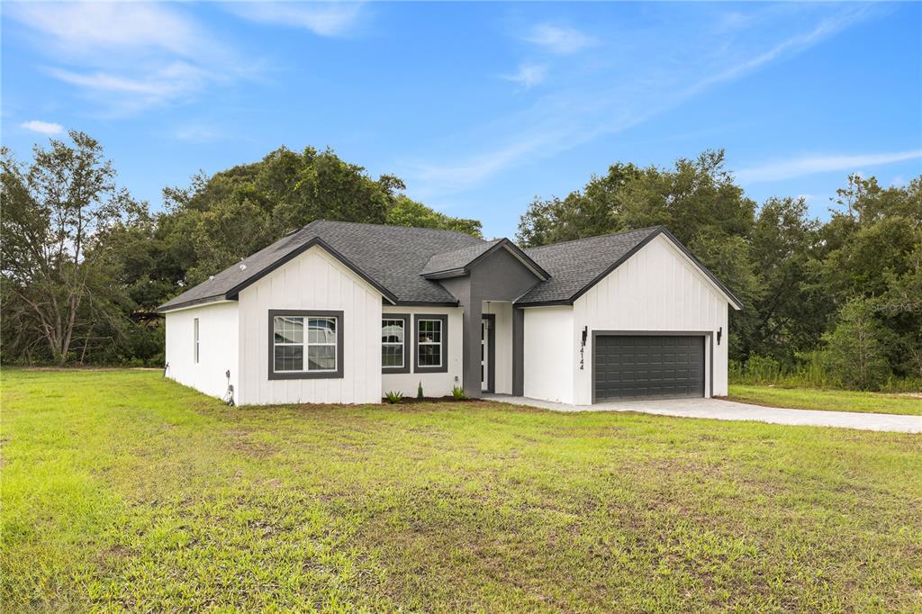 A modern white farmhouse with a dark gray roof and garage sits on a grassy lot — 14144 SW 47 AVENUE, OCALA, FL